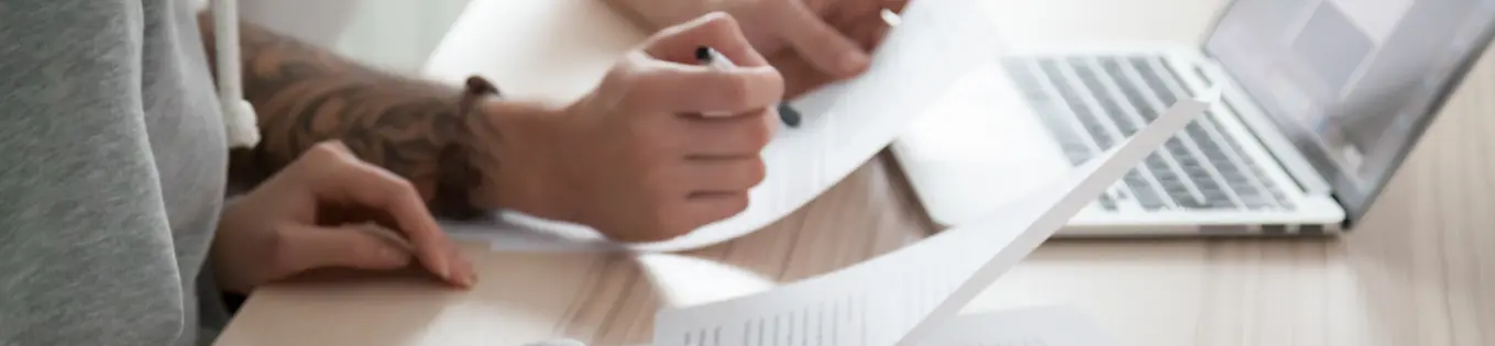 Person inspecting a printout with a laptop in the background
